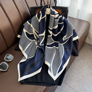 Elegant navy and beige silk scarf with geometric leaf pattern draped on a handbag