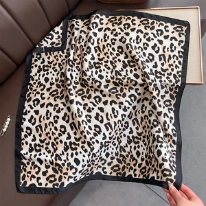 Detail view of leopard print silk-like scarf with black borders on brown leather