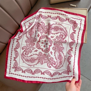 Detailed view of square silk scarf with red paisley print on brown leather surface