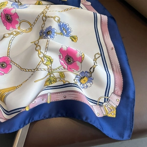 Detail of silk satin scarf with floral poppy print and golden chain motifs on leather