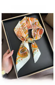 Detail of a silky paisley satin square scarf with orange and green patterns in a tray