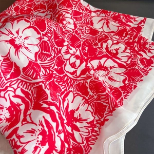 Close-up of silk-textured floral scarf featuring elegant red and white print with rolled hem
