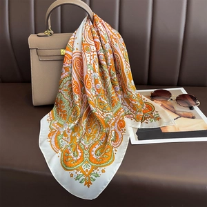 Orange paisley silk scarf draped on a leather bag with sunglasses and magazine