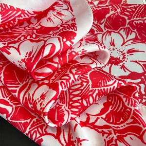 Close-up of silk-like satin fabric with elegant red tropical floral prints and soft sheen