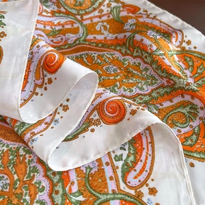 Detailed macro view of paisley pattern silk scarf with hand-rolled edges on wood