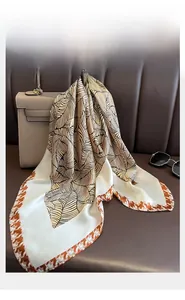 Dettaglio di sciarpa in seta con foglie nere e bordo pied de poule arancione su una borsa