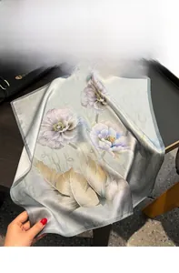 Vue détaillée d'un foulard en soie aux motifs vintage de fleurs et plumes sur un plateau
