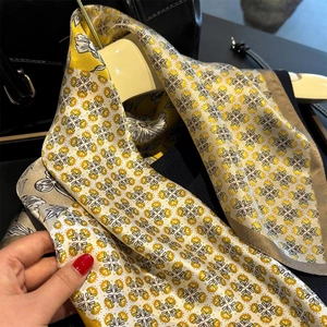 Détail d'un foulard en soie à fleurs géométriques jaunes suspendu sur cintre