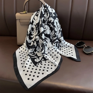 Seidenschal mit Punkten und Kamelien-Muster, elegant auf einer Ledertasche drapiert