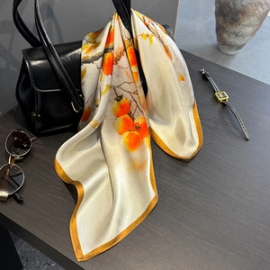 Elegant silk scarf with orange persimmon print draped over a black leather handbag