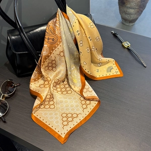 Eleganter Seidenschal in Orange mit Paisley-Muster auf einer schwarzen Lederhandtasche