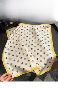 Macro shot of silk scarf with floral print and yellow edge against a black leather bag