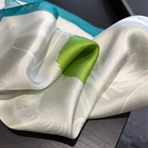 Close-up of silk scarf showing glossy satin texture and teal botanical print edge