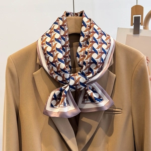 Close-up of geometric pattern silk scarf styled with a knot on a camel blazer