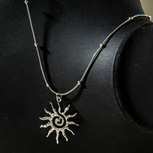 Vue rapprochée du collier soleil argenté avec texture spirale sur support en velours
