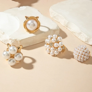 Detailed view of gold alloy baroque pearl rings and earrings on a textured stone surface