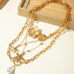 Detailed close-up of multilayer gold necklace with starfish, flowers, and pearl pendants