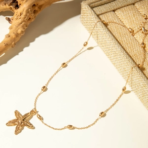 Close-up of golden starfish necklace with metallic beads on a natural minimalist background