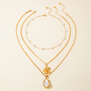 Close-up of triple layered gold necklace set with baroque pearl and floral charms