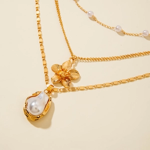 Macro shot of layered gold necklace with irregular white pearl and floral charm detail