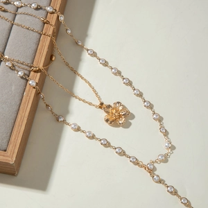 Detail of layered gold necklace featuring a 3D flower pendant and a delicate pearl chain