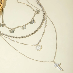 Detail of multi-layer silver necklace with butterfly, shell and cross charms