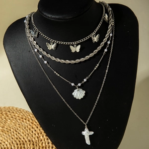 Detail of layered silver necklaces featuring butterfly, shell, and pearl charms on a display