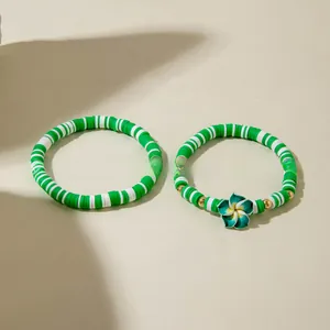 Détail de bracelets bohèmes en pâte polymère avec breloque fleurie verte et motifs rayés