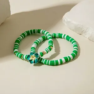 Détail de bracelets en perles heishi vertes et blanches avec pendentif fleuri et or