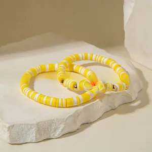 Détail du pendentif fleur jaune et bracelets en perles heishi en argile sur pierre