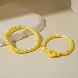 Détail de bracelets en perles Heishi jaunes et blanches avec breloque fleur de frangipanier