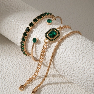 Gros plan d'un ensemble de 4 bracelets dorés avec des pierres précieuses vert émeraude