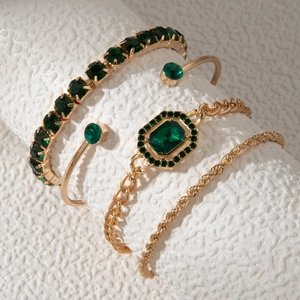 Détail d'un ensemble de 4 bracelets dorés ornés de strass vert émeraude sur fond texturé