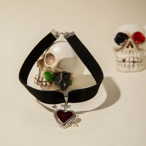 Choker gothique en velours avec pendentif cœur rouge percé et croix sur un crâne blanc