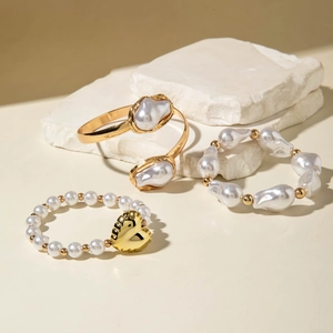 Close-up of golden metal cuff with baroque pearls and a heart pendant charm bracelet