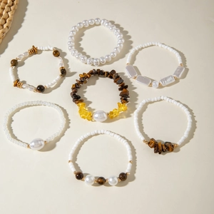 Set of seven beaded bracelets with pearl, tiger eye, and citrine stones on a minimal surface