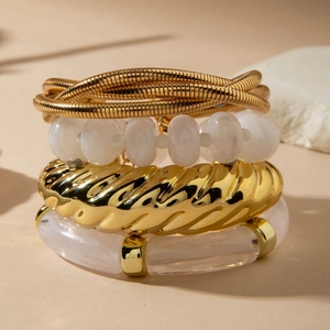 Detail of four-piece gold and white beaded layered bracelet set with metallic textures