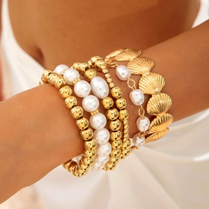 Detailed view of layered gold bead bracelets and baroque pearls on a model wrist