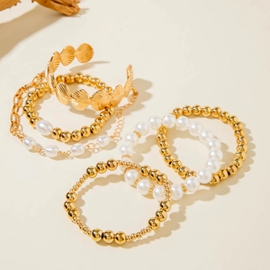 Detail of bohemian gold bead bracelets and shell texture metal bangle set on stone surface