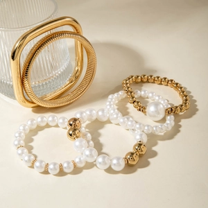 Detail of gold liquid metal bangle and pearl beaded bracelet set on minimalist background