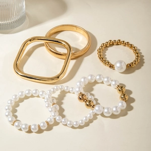 Detail shot of five-piece gold bangle set with irregular metal texture and white pearls