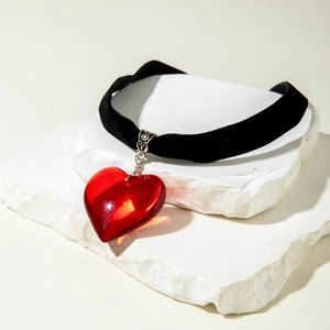 Macro shot of large red glass heart pendant on black velvet choker over white stone