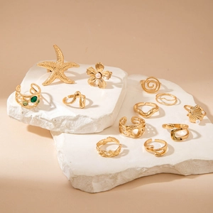 Set of 11 gold starfish and flower rings with green stones on white stone stands