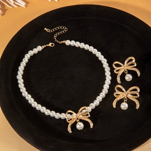 Set collana di perle eleganti con fiocchi dorati e orecchini abbinati su velluto nero