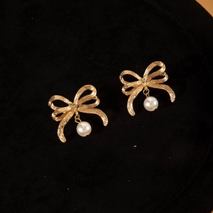 Dettaglio di orecchini a fiocco vintage con metallo dorato spazzolato e perle su velluto nero