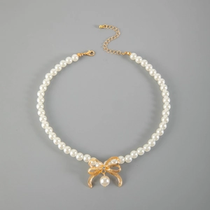 Collana di perle con ciondolo a fiocco dorato e pietra brillante su sfondo grigio puro
