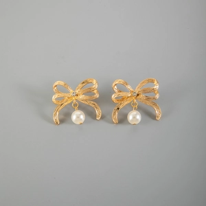 Orecchini a fiocco dorati con strass e perle bianche su sfondo grigio minimalista