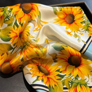Gros plan détaillé montrant l'imprimé tournesol et la texture soyeuse du foulard carré