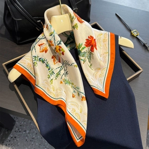 Carré en soie aux motifs floraux et bordure orange drapé sur un vêtement en maille bleue