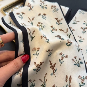 Dettaglio di un foulard in seta floreale con bordo nero e trama in raso